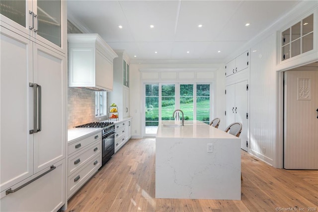 kitchen with high end black range, white cabinets, a center island with sink, and light hardwood / wood-style flooring