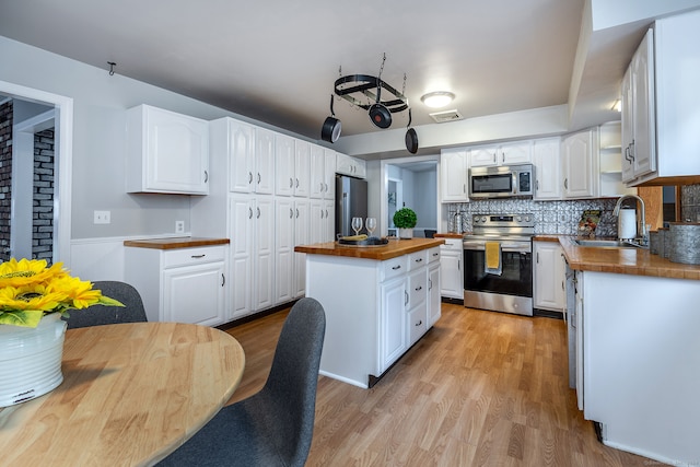 kitchen featuring white cabinetry, stainless steel appliances, a center island, light wood-type flooring, and wood counters