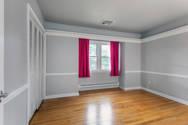 unfurnished bedroom featuring a baseboard heating unit and wood-type flooring