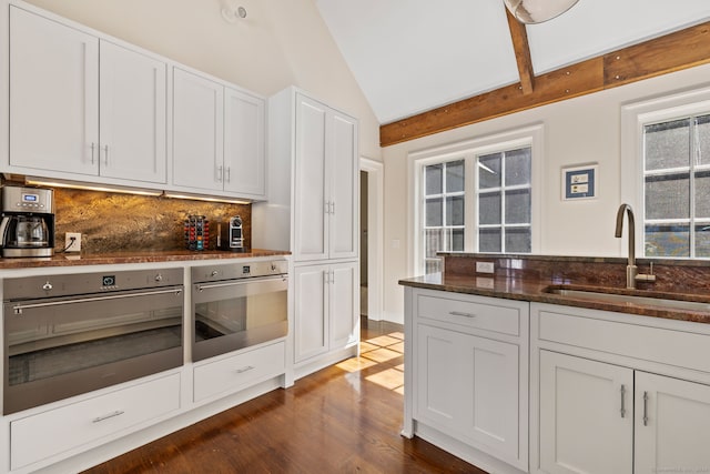 kitchen with dark wood-type flooring, sink, vaulted ceiling, white cabinetry, and stainless steel oven