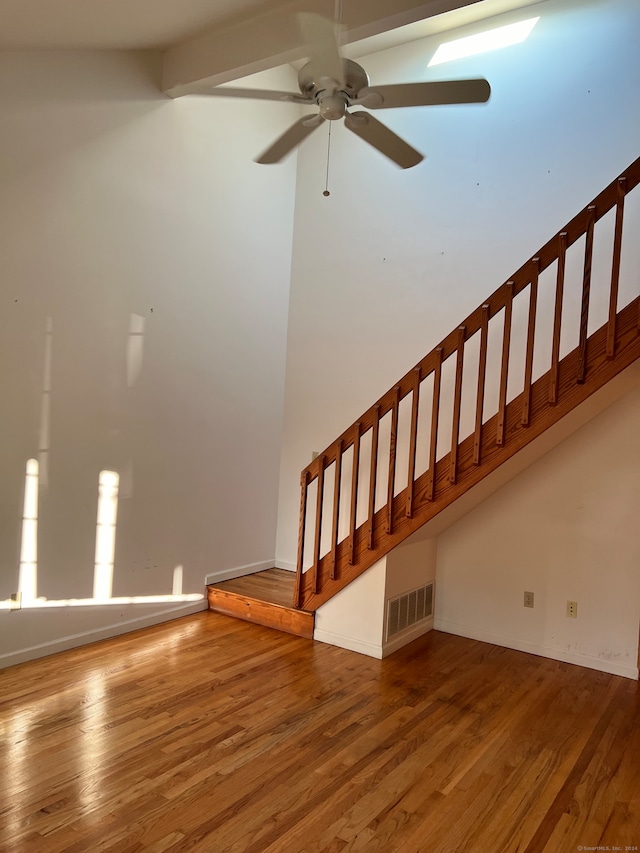 staircase with ceiling fan, beam ceiling, and wood-type flooring