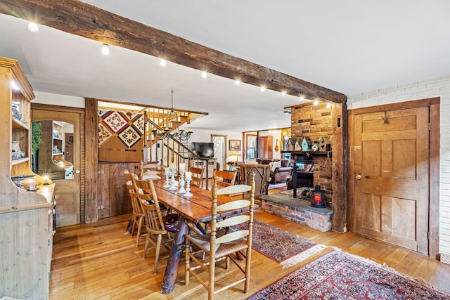 dining room featuring light wood-type flooring, wood walls, beamed ceiling, and brick wall