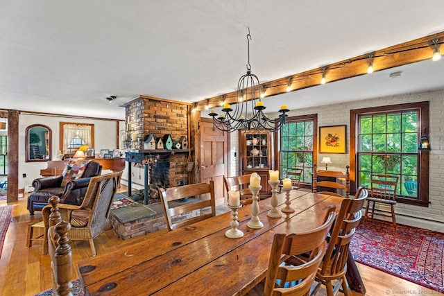 dining area with a baseboard radiator, brick wall, a brick fireplace, a notable chandelier, and light wood-type flooring