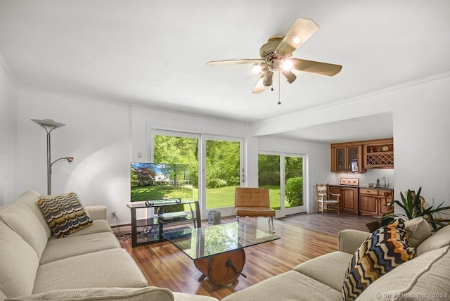 living room with wood-type flooring, ornamental molding, bar area, and ceiling fan