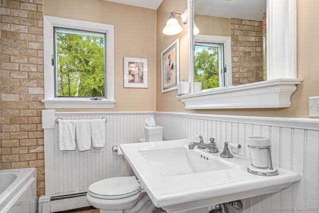 bathroom with a baseboard heating unit, a wealth of natural light, toilet, and a bathing tub