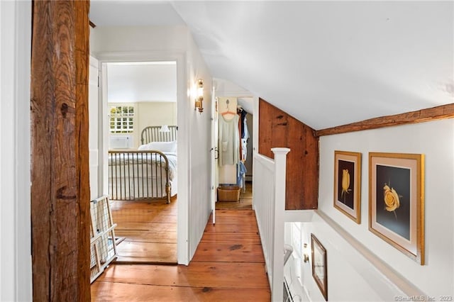 corridor with light hardwood / wood-style flooring, vaulted ceiling, and baseboard heating