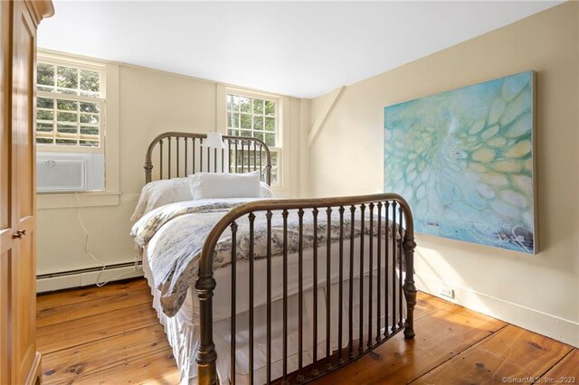 bedroom with cooling unit, a baseboard radiator, and wood-type flooring