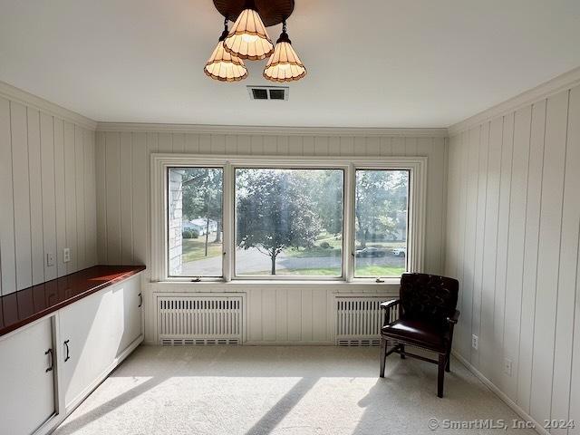 sitting room with wooden walls, crown molding, radiator, and light carpet