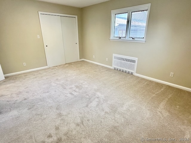 unfurnished bedroom featuring carpet floors, a closet, and radiator heating unit