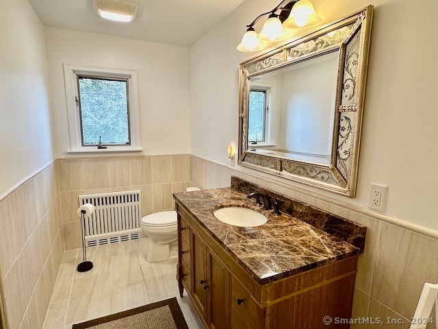 bathroom featuring radiator, vanity, toilet, tile walls, and tile patterned flooring