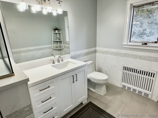 bathroom featuring tile walls, vanity, tile patterned flooring, radiator, and toilet