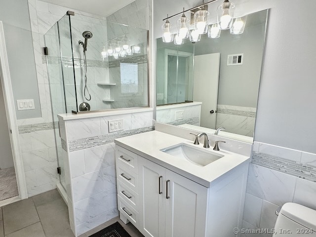 bathroom featuring tile walls, vanity, tile patterned flooring, a shower with door, and toilet