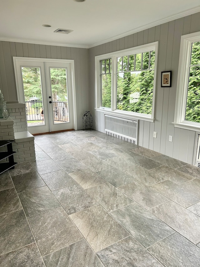 unfurnished living room with french doors, crown molding, wood walls, and radiator heating unit