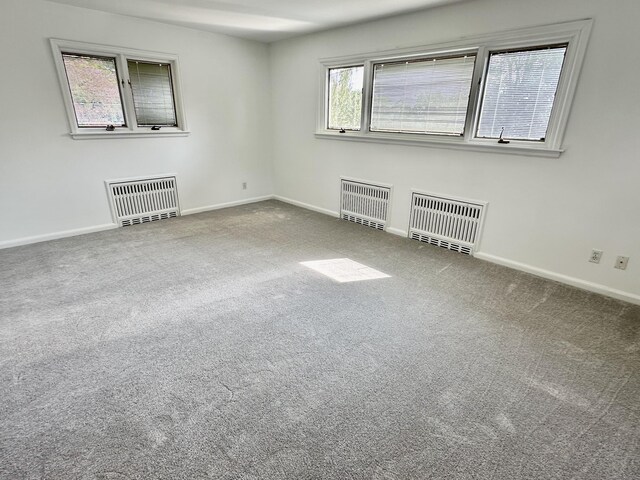 carpeted spare room featuring radiator, heating unit, and a healthy amount of sunlight