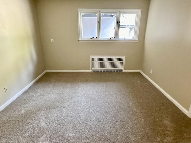 unfurnished room featuring carpet and radiator heating unit