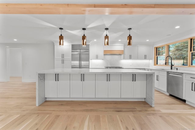 kitchen with light stone counters, stainless steel appliances, decorative light fixtures, sink, and a spacious island