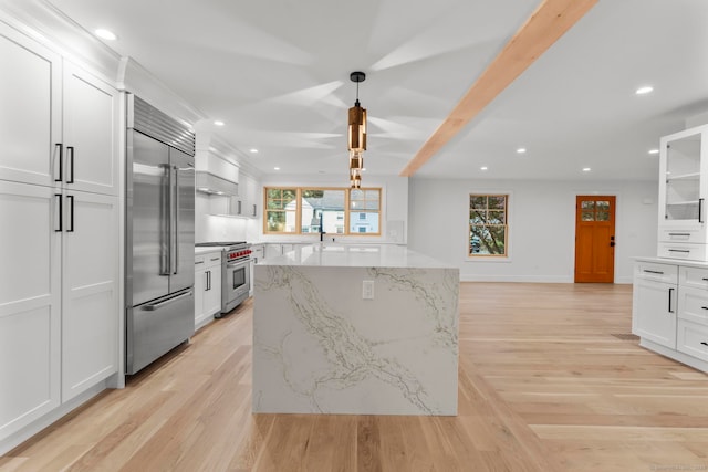 kitchen with high quality appliances, white cabinetry, light stone counters, and light hardwood / wood-style flooring