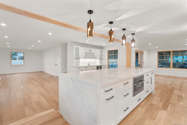 kitchen with white cabinetry, a spacious island, stainless steel oven, and decorative light fixtures