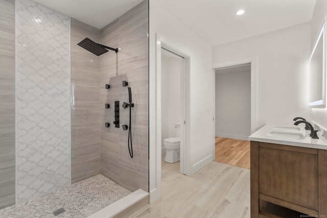 bathroom featuring toilet, vanity, hardwood / wood-style floors, and a tile shower