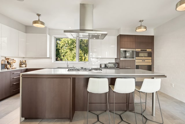 kitchen with white cabinets, island range hood, dark brown cabinets, decorative light fixtures, and stainless steel appliances