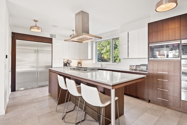 kitchen with white cabinets, island exhaust hood, built in appliances, a center island, and a breakfast bar area