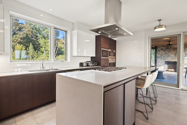 kitchen with dark brown cabinetry, white cabinets, sink, island range hood, and a fireplace