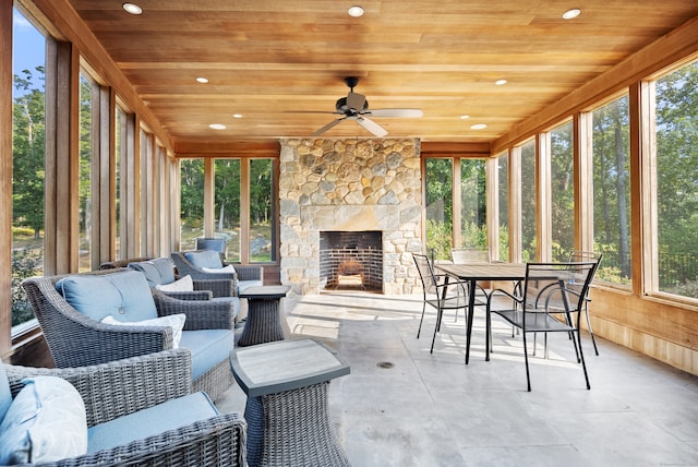 sunroom / solarium with an outdoor stone fireplace, wooden ceiling, and ceiling fan