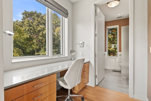 office with light hardwood / wood-style flooring, built in desk, and a healthy amount of sunlight