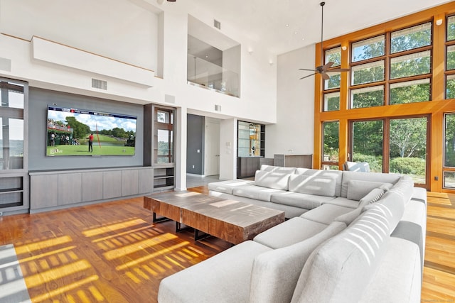 living room with a healthy amount of sunlight, a towering ceiling, ceiling fan, and hardwood / wood-style flooring