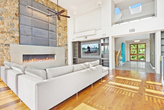 unfurnished living room with a large fireplace, light hardwood / wood-style floors, ceiling fan, and a high ceiling