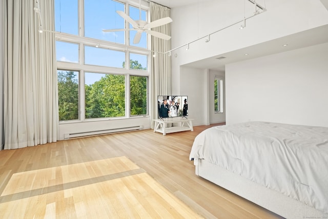 bedroom featuring hardwood / wood-style floors, a towering ceiling, a baseboard heating unit, and ceiling fan