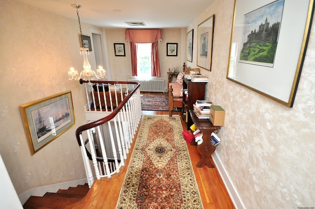 hallway with light wood-type flooring, radiator heating unit, and a notable chandelier