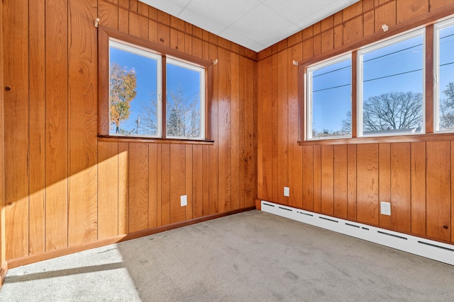 empty room featuring carpet flooring, a wealth of natural light, wooden walls, and a baseboard radiator