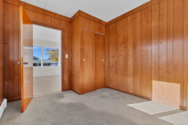 unfurnished room featuring light carpet, baseboard heating, and wooden walls