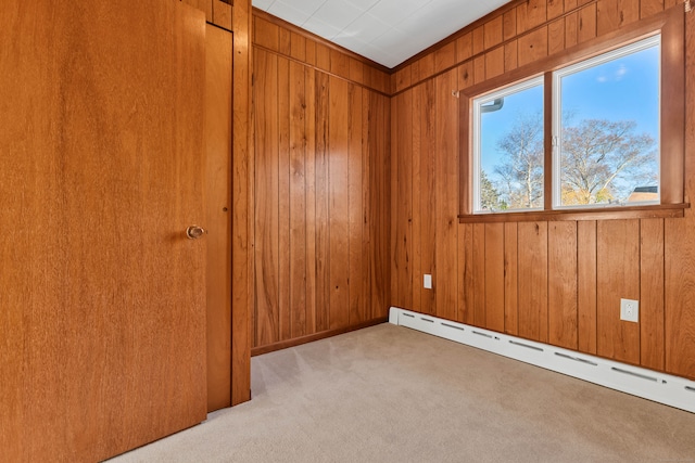 spare room featuring baseboard heating, wood walls, and light carpet