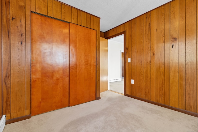 unfurnished bedroom with light colored carpet, a textured ceiling, wooden walls, and a closet