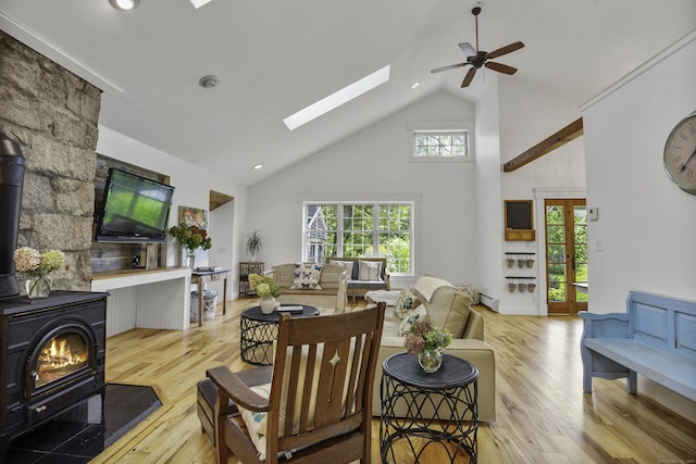 living room with a wood stove, ceiling fan, a skylight, light hardwood / wood-style flooring, and high vaulted ceiling