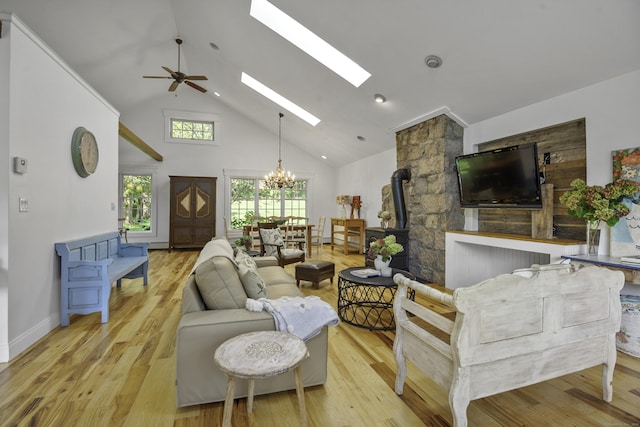 living room with a wood stove, high vaulted ceiling, light hardwood / wood-style floors, and ceiling fan with notable chandelier