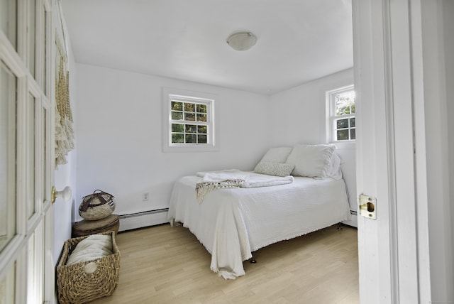 bedroom featuring light hardwood / wood-style floors, baseboard heating, and multiple windows