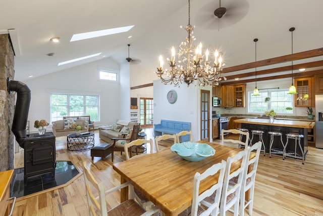 dining space with a skylight, ceiling fan with notable chandelier, high vaulted ceiling, light hardwood / wood-style floors, and a wood stove