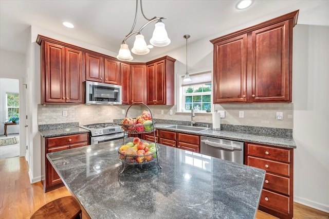 kitchen featuring appliances with stainless steel finishes, a kitchen island, pendant lighting, light hardwood / wood-style flooring, and sink