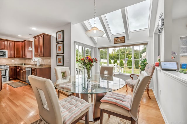 dining room with sink, light hardwood / wood-style flooring, and lofted ceiling with skylight