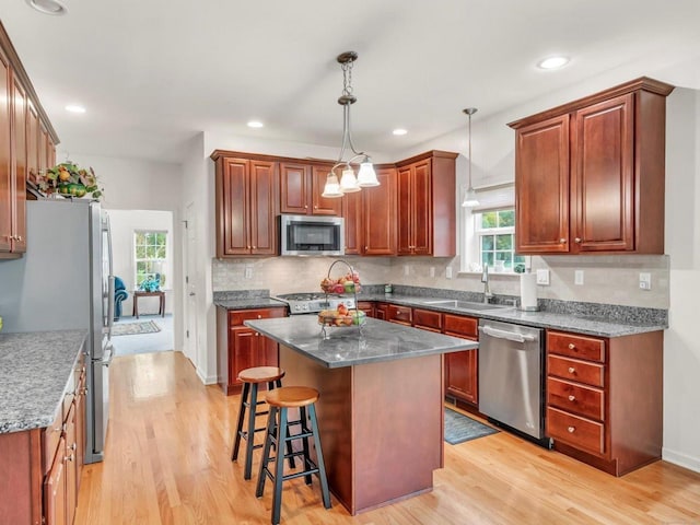 kitchen featuring light wood-type flooring, a center island, sink, hanging light fixtures, and appliances with stainless steel finishes