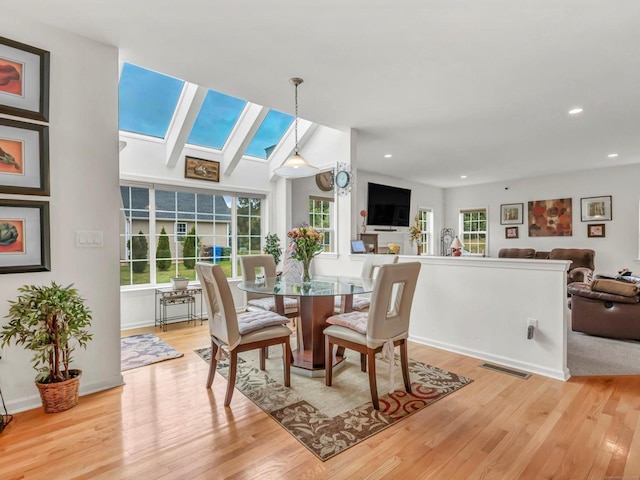 dining area featuring light hardwood / wood-style floors and lofted ceiling with skylight