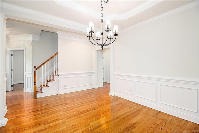 unfurnished dining area featuring a tray ceiling, crown molding, wood-type flooring, and an inviting chandelier