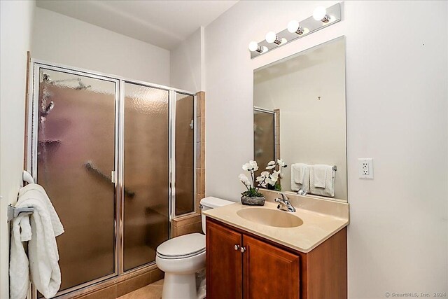 bathroom with tile patterned floors, a shower with door, vanity, and toilet