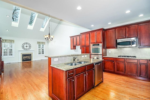 kitchen featuring sink, stainless steel appliances, light hardwood / wood-style flooring, decorative light fixtures, and vaulted ceiling with skylight