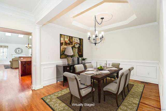 dining room featuring ornate columns, a notable chandelier, crown molding, hardwood / wood-style floors, and a tray ceiling