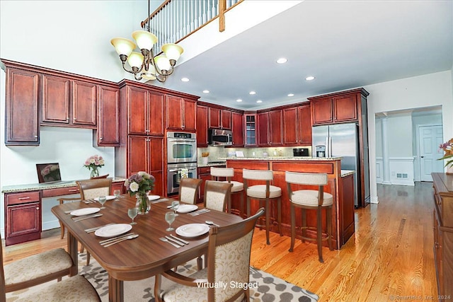 kitchen featuring appliances with stainless steel finishes, light wood-type flooring, an inviting chandelier, a kitchen island, and hanging light fixtures