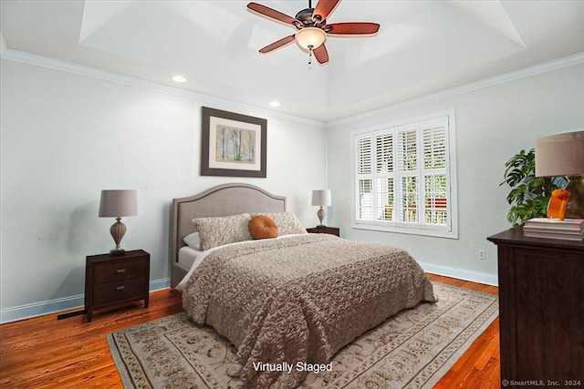 bedroom featuring ceiling fan, a raised ceiling, wood-type flooring, and ornamental molding